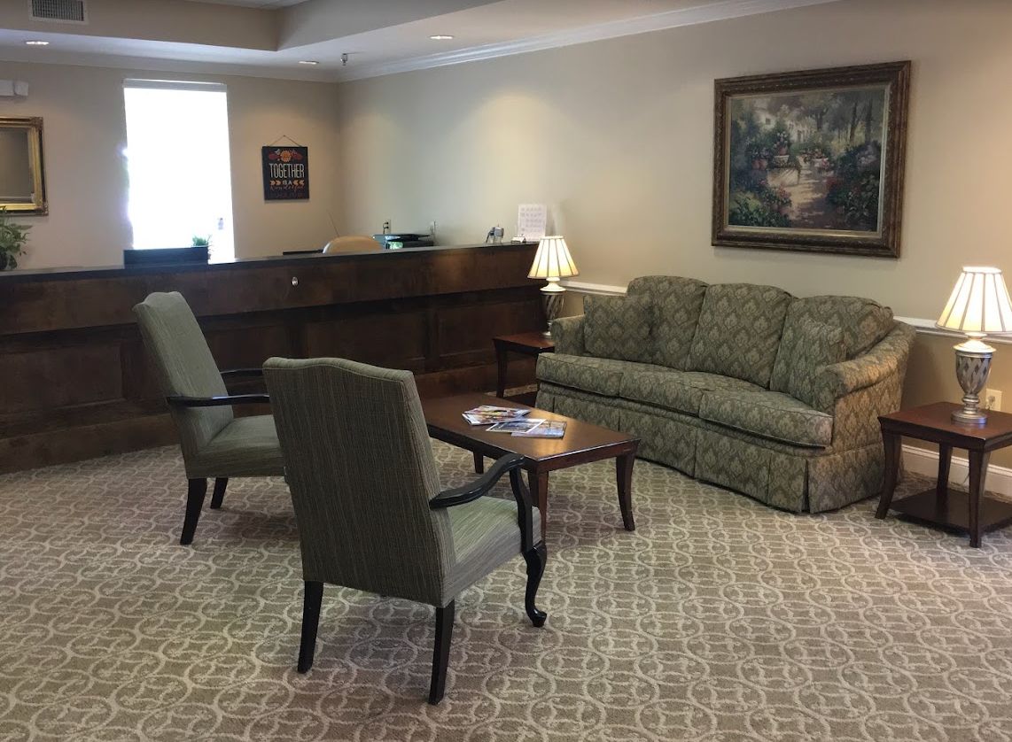 A cozy waiting room featuring a sofa, chairs, and a wooden desk with a lamp.
