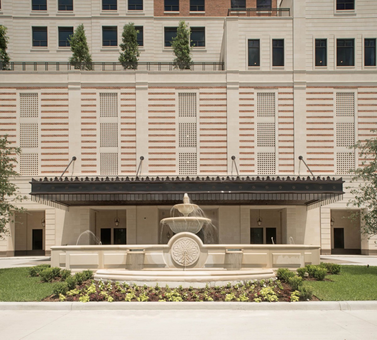 A view of an elegant building facade with a central fountain and landscaped surroundings.
