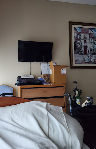 A view of a hospital room featuring a TV, wooden furniture, and a piece of artwork on the wall.