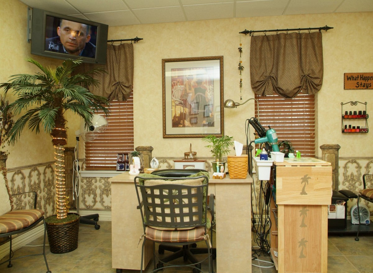 An interior view of a nail salon featuring a work desk, a chair, and decorative elements such as plants and artwork.