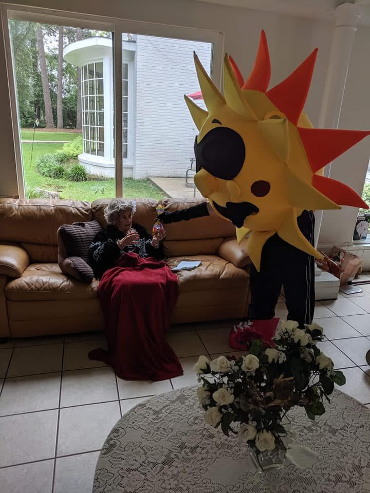 A person in a sun costume interacts with someone sitting on a sofa in a living room.