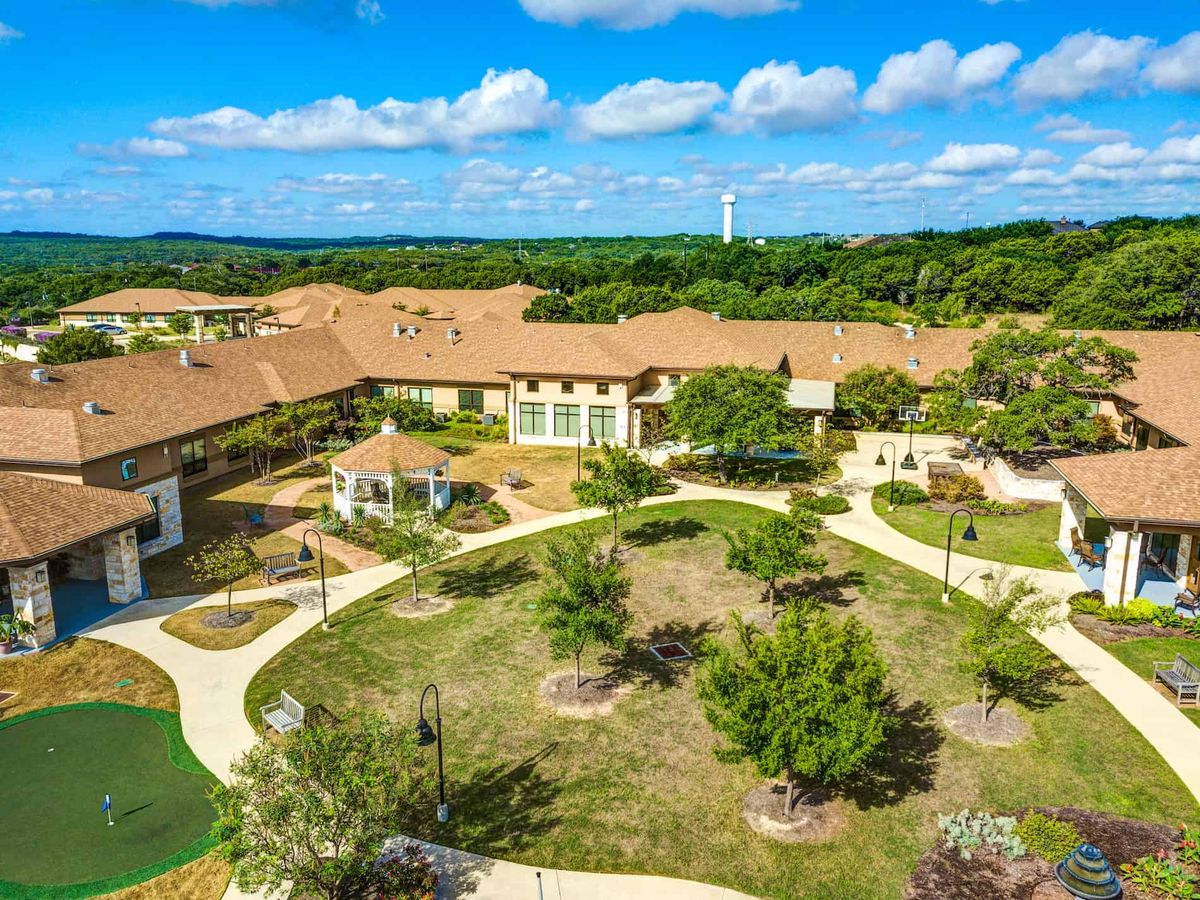 Aerial view of a large building complex surrounded by lush greenery and winding pathways under a bright blue sky.