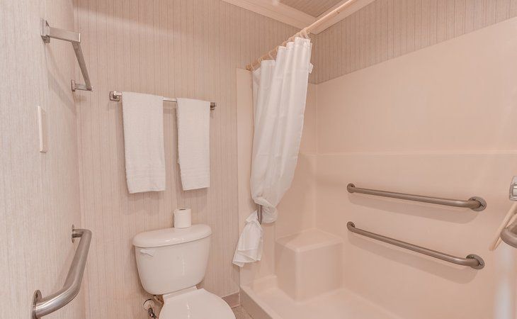A clean bathroom with towels, a toilet, and a shower area equipped with grab bars.