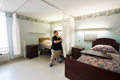 A nurse adjusts the privacy curtain in a patient room within a healthcare facility.