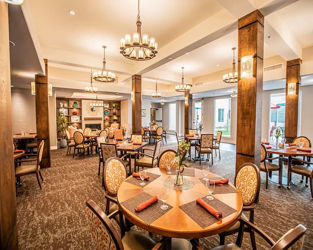 A spacious and elegantly decorated dining room with multiple tables and chairs, enhanced by warm lighting from chandeliers.