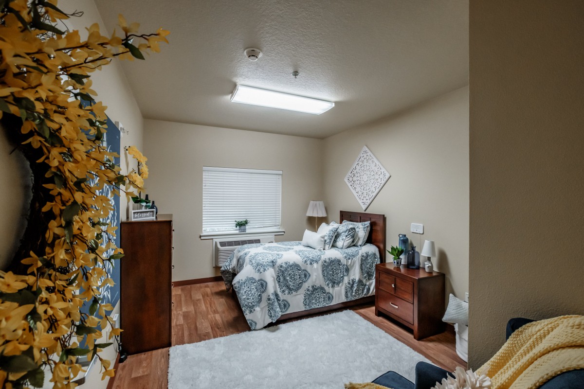 A cozy bedroom with a neatly made bed, wooden furniture, and soft lighting.