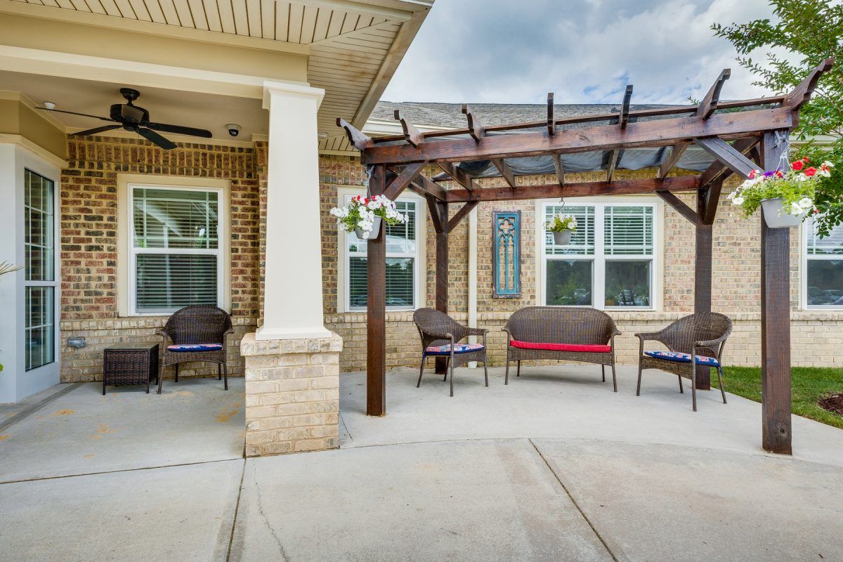 A cozy patio area with outdoor seating under a pergola attached to a brick building.
