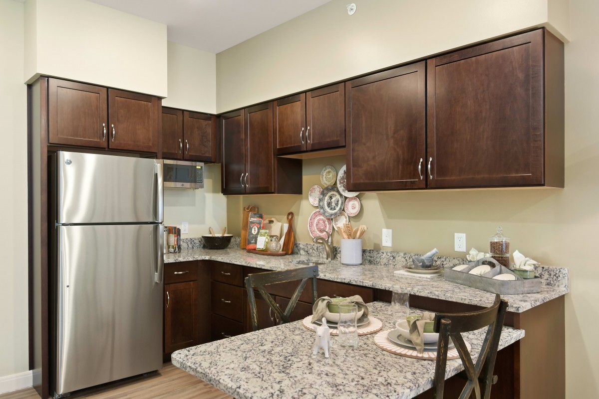 A modern kitchen with dark wooden cabinetry, a granite countertop, and stainless steel appliances.