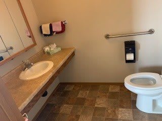 A bathroom with a sink, mirror, and toilet, featuring tiled flooring and a handrail.