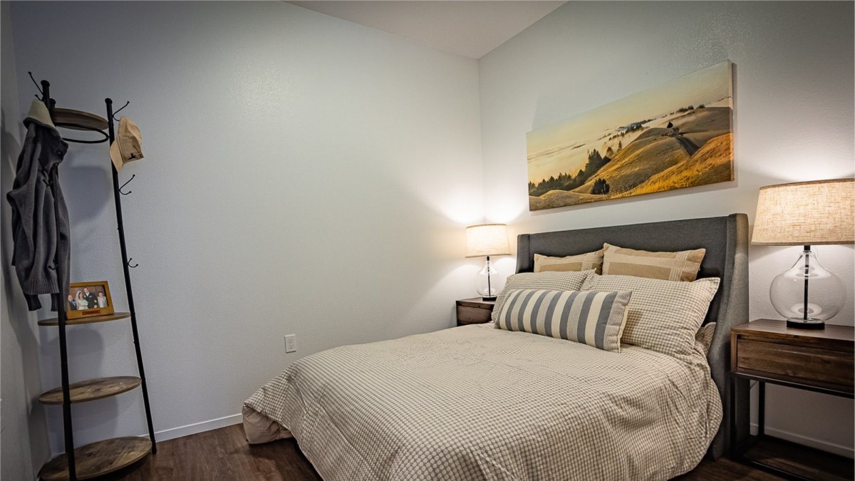 A cozy bedroom with a neatly made bed, featuring decorative pillows and a bedside lamp, under a landscape painting.
