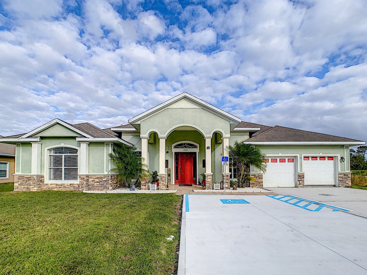 A suburban house with a red front door and a spacious driveway under a cloudy sky.