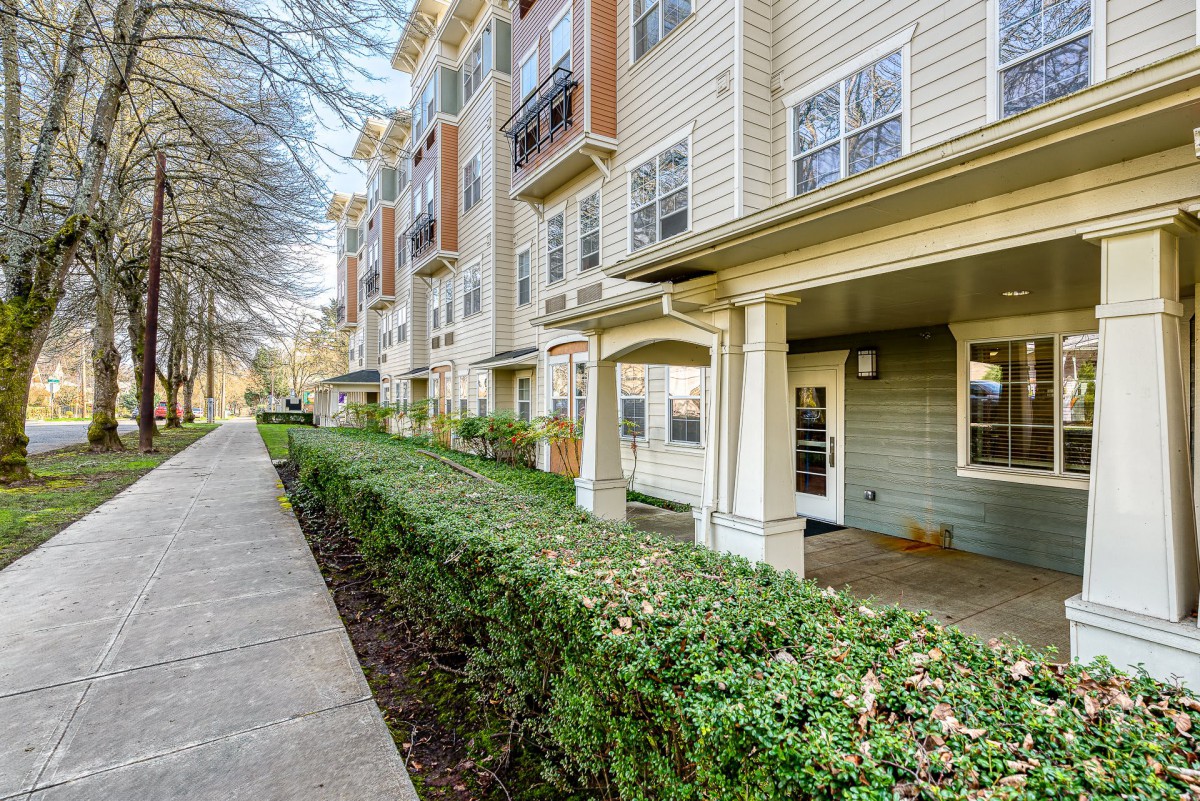 A modern apartment building with well-maintained landscaping and a sidewalk in the foreground.