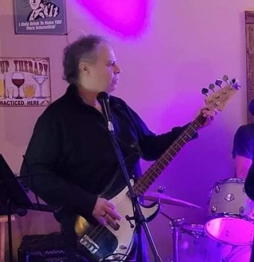 A musician playing bass guitar during a live performance, illuminated by purple lights.