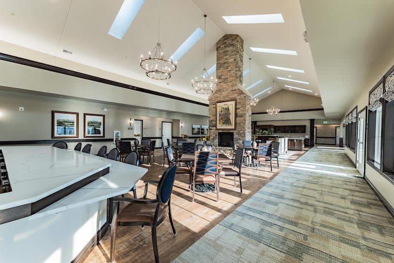 A spacious, well-lit restaurant interior featuring a central fireplace and elegant chandeliers.