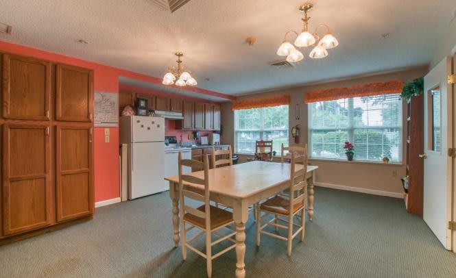 A cozy kitchen and dining area with a wooden table, chairs, and ample natural light from large windows.