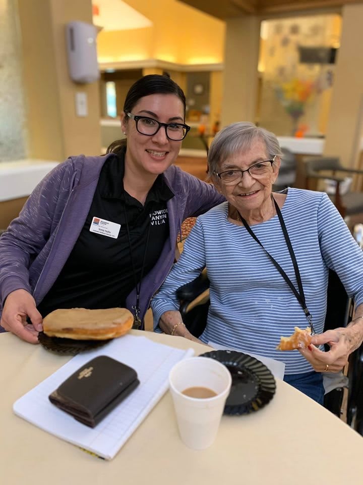 A caregiver and an elderly person enjoying a meal together indoors.