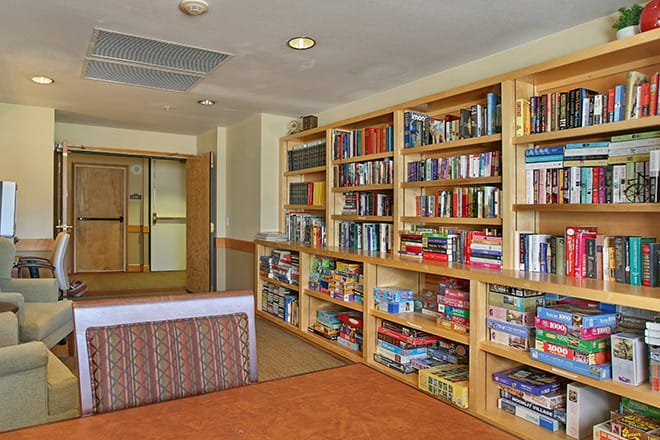 A cozy library space featuring wooden bookshelves filled with books and board games.