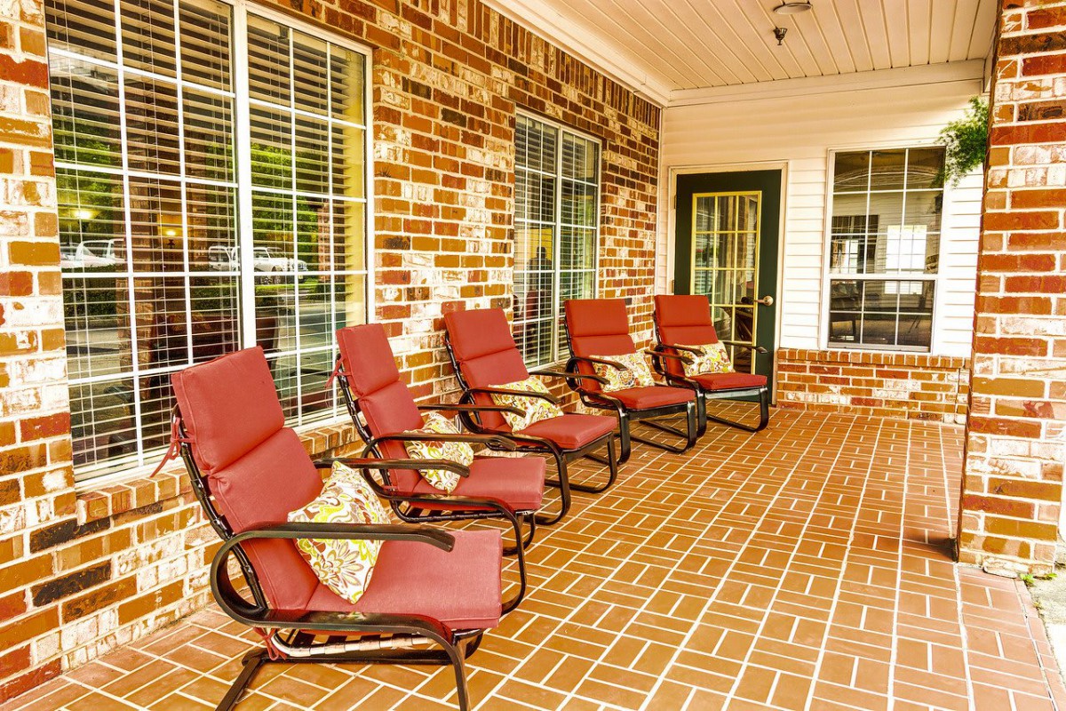 A cozy porch with red-cushioned chairs lined up against a brick wall.