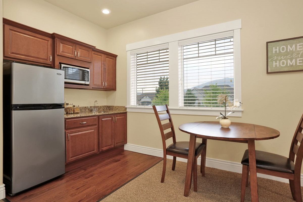 A cozy kitchen and dining area with wooden cabinets, a small round table, and two chairs by the window.