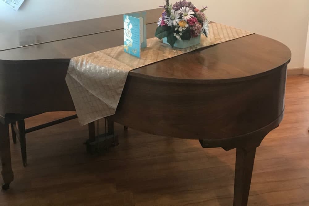 A decorative grand piano adorned with a table runner and a vase of flowers.