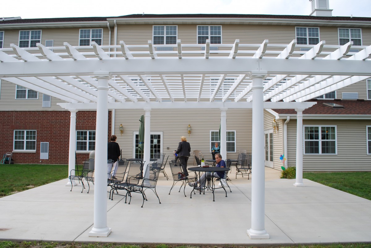 An outdoor patio area featuring a white pergola and metal furniture in front of a building.