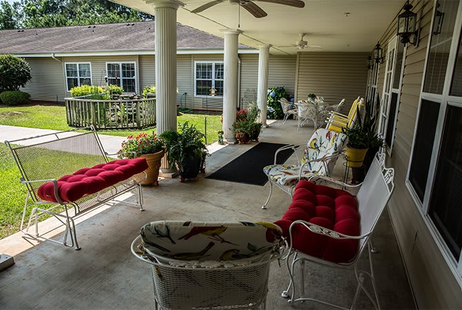 A cozy outdoor patio area with cushioned seating, plants, and a covered porch.