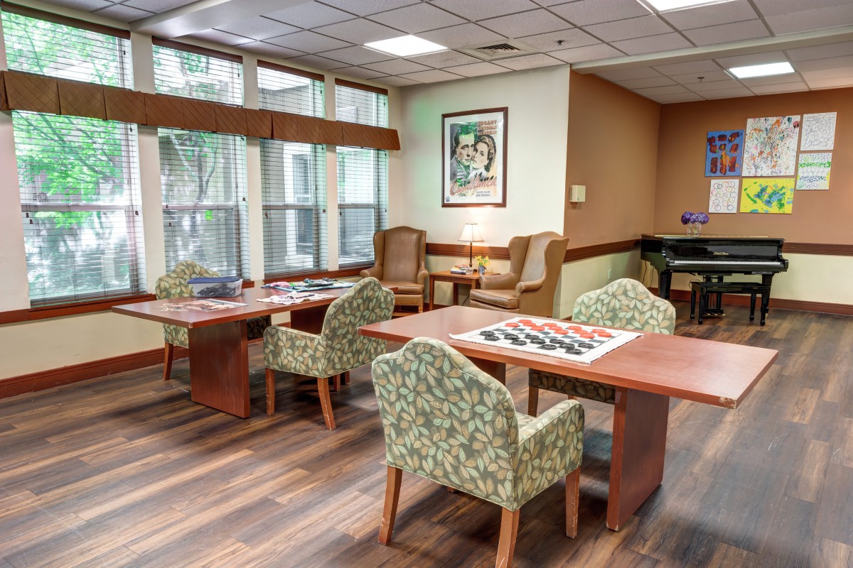 A cozy lounge area with tables and upholstered chairs, featuring a game board on one table and large windows providing natural light.