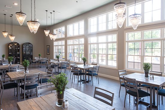 A bright and modern restaurant interior featuring large windows, elegant chandeliers, and neatly arranged tables and chairs.