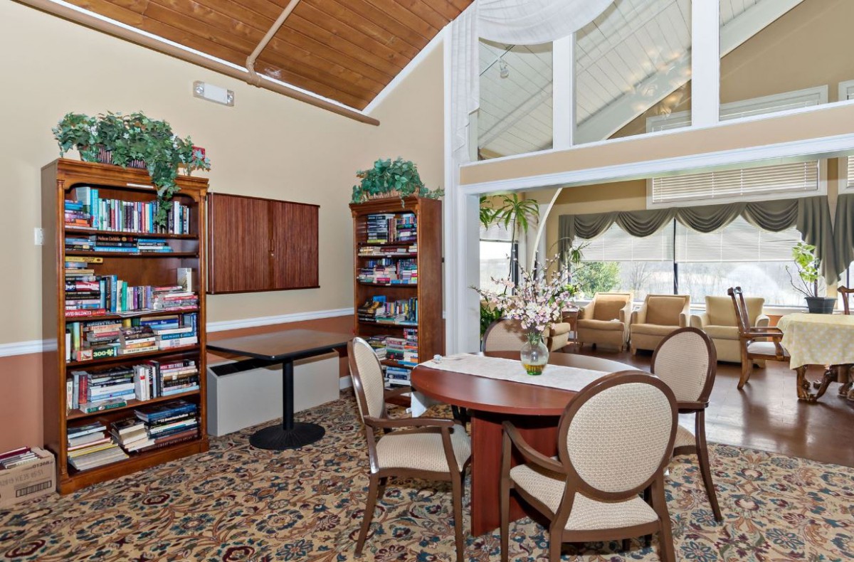A cozy library corner with bookshelves, a table, and chairs next to large windows.