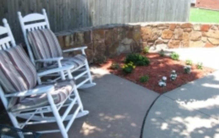 A cozy patio area featuring a rocking chair and a small garden.