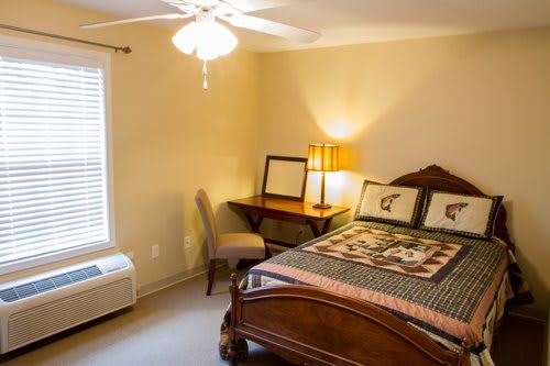 A cozy bedroom with a bed, desk, and chair, softly lit by a lamp.