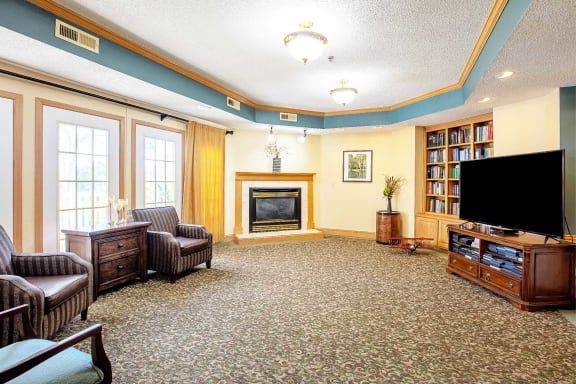 A cozy living room with a fireplace, armchair, television, and large windows.