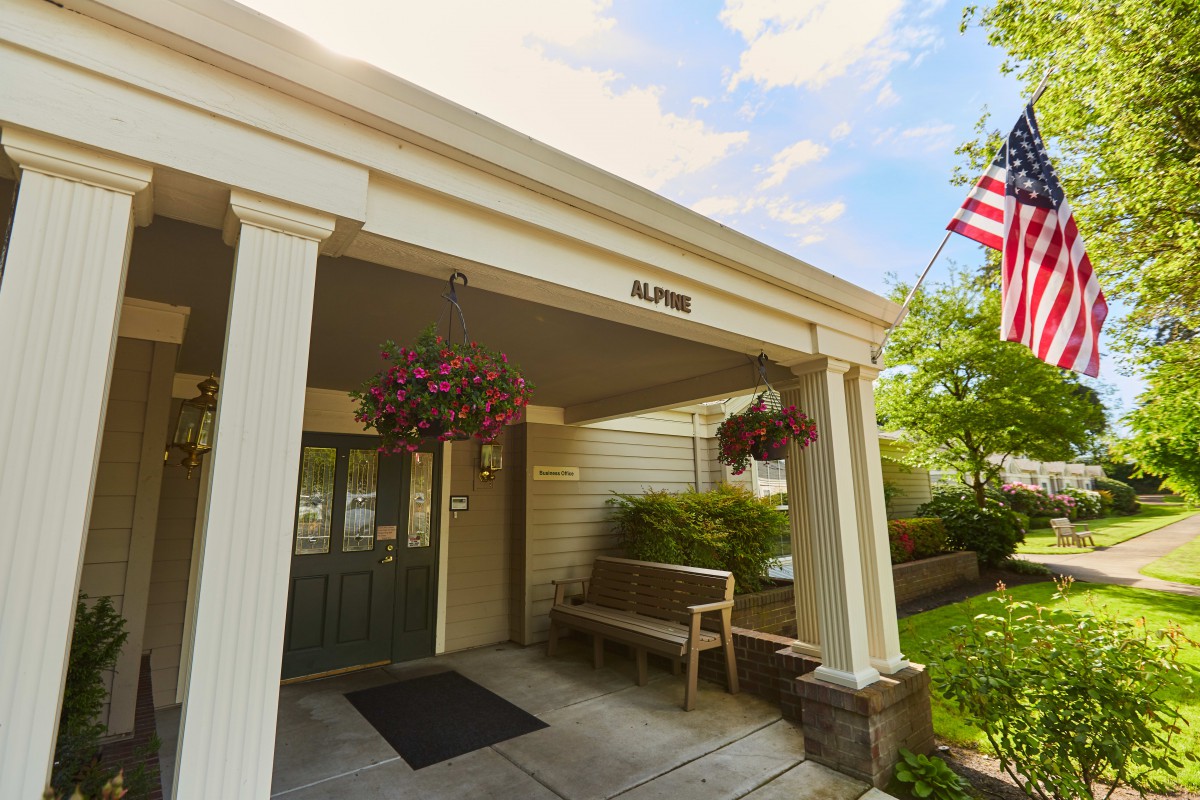 An inviting building entrance with columns, a bench, hanging plants, and an American flag.