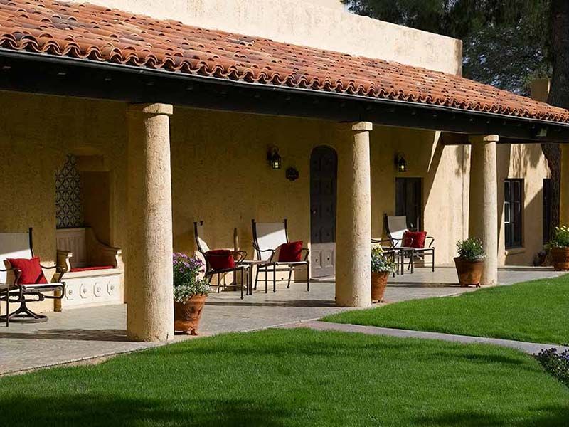 A beautiful house with a shaded porch, featuring columns and comfortable patio seating, overlooks a lush green lawn.