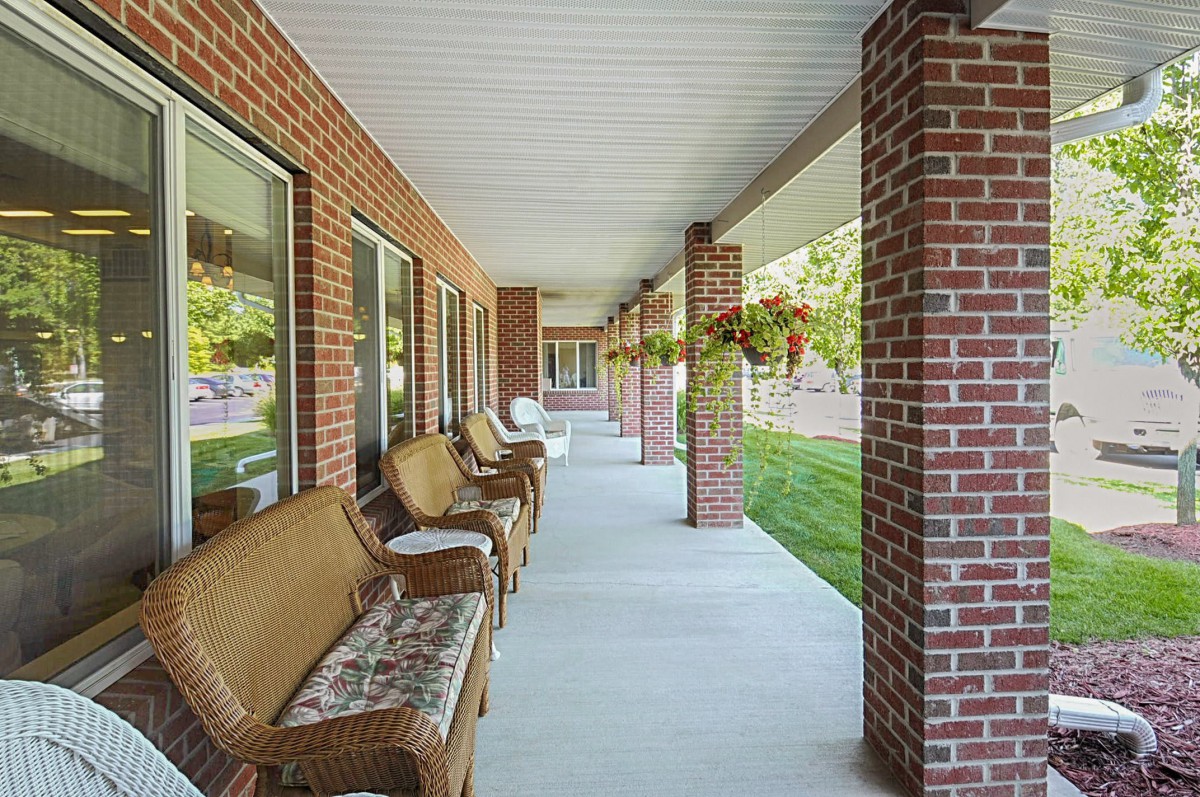 A long covered porch with brick pillars, benches, and hanging plants.