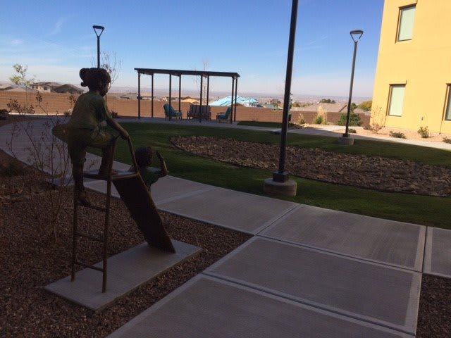 A sculpture of a person on a bench in an outdoor park setting with walkways and distant landscape views.