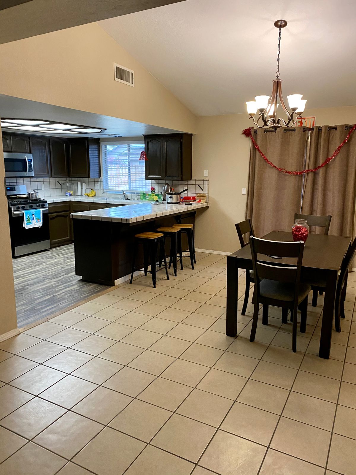 A modern open-concept kitchen and dining area with an island and seating, featuring a chandelier and tiled flooring.