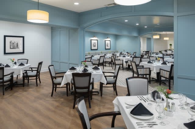 An elegant restaurant dining room with neatly arranged tables and chairs, set with white tablecloths and folded napkins.