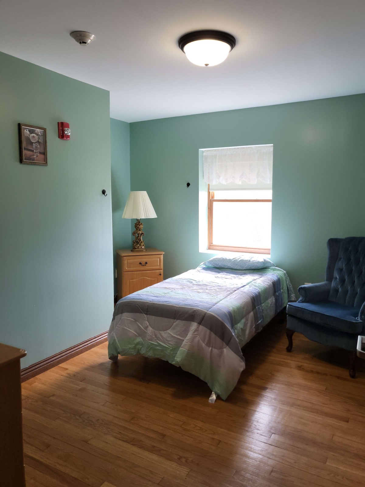 A simple bedroom with a single bed, blue chair, and wooden furniture.