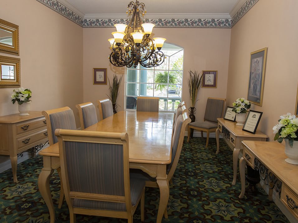 A formal dining room featuring a large wooden table, elegant chandelier, and decorative plants.