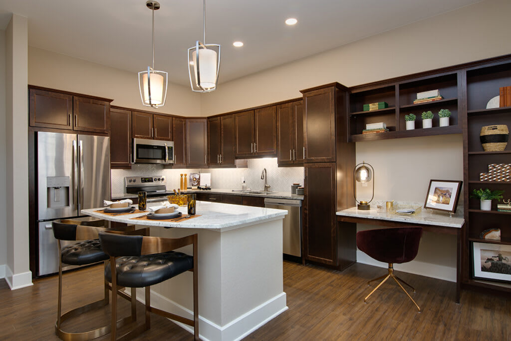 A modern kitchen with dark wood cabinets and an island, featuring pendant lights and stainless steel appliances.