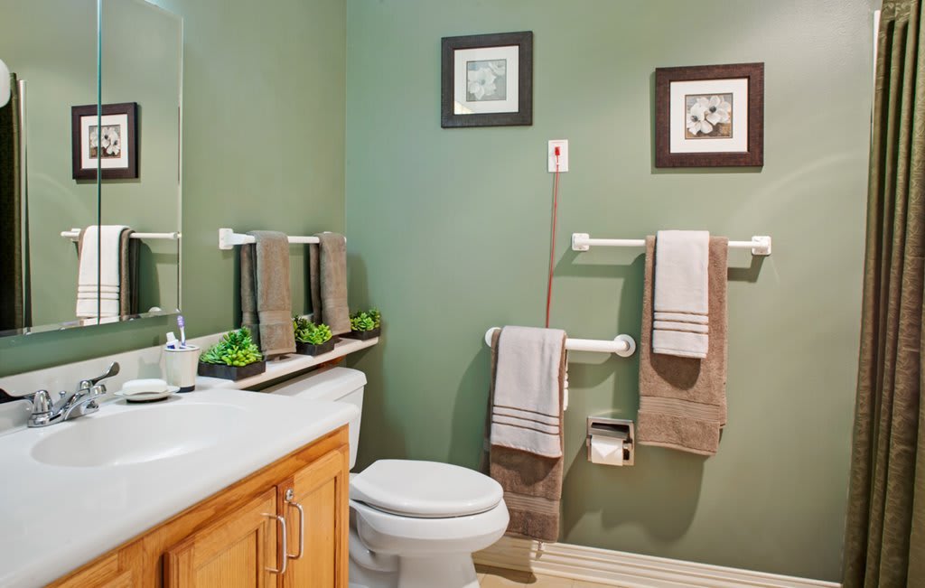 A neatly organized bathroom with green walls, featuring a toilet, sink, and towels on display.