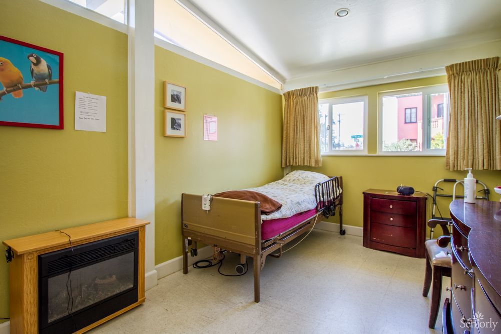 A simple hospital room with yellow walls, featuring a bed and a window.