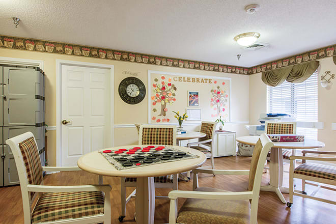 A cozy community game room featuring tables with checkers boards, comfortable chairs, and decorative elements.