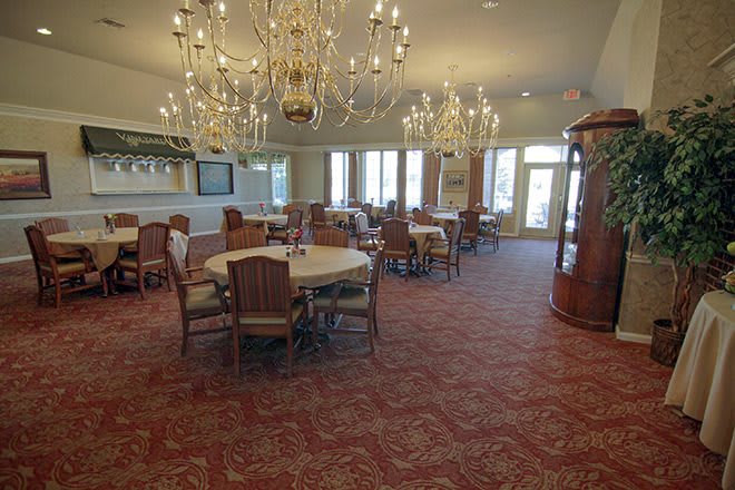 An elegant dining room featuring chandeliers, round tables with chairs, and a patterned carpet.