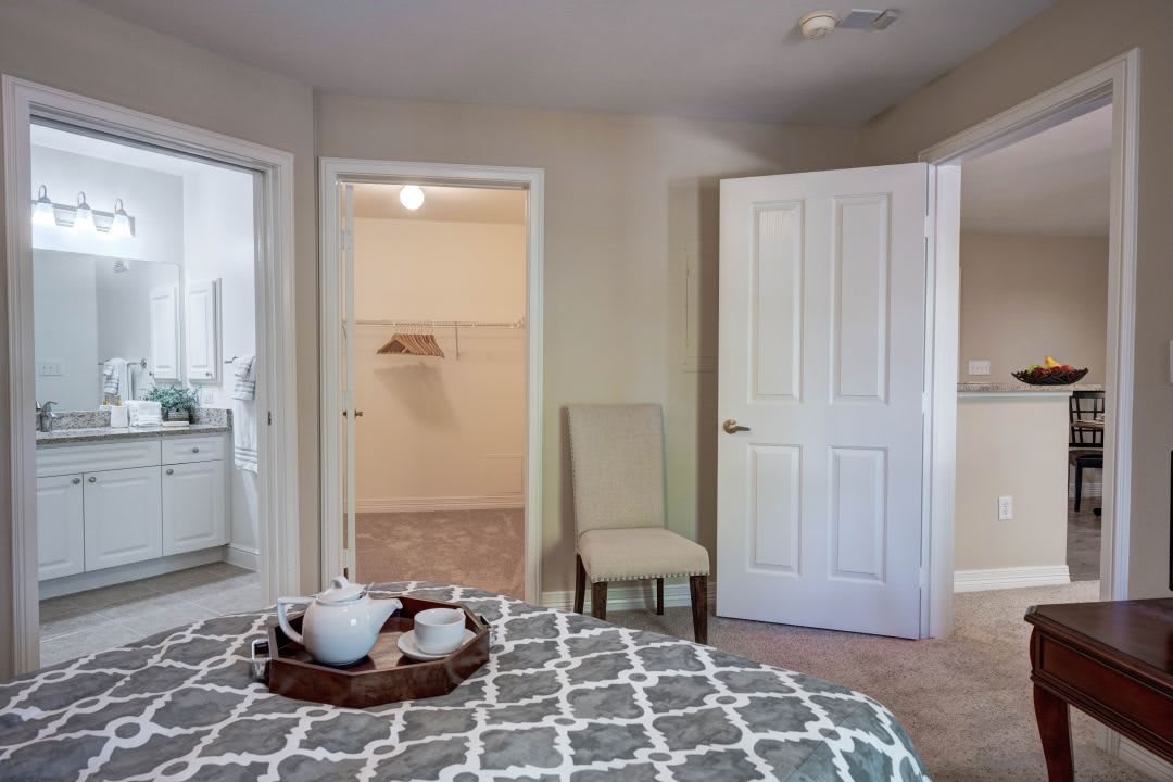 A cozy bedroom with a patterned bedspread, an open closet, and a tray with teacups.