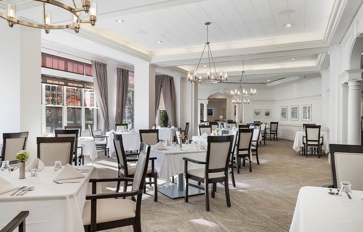 An elegant dining room with neatly arranged tables and chairs, complemented by stylish chandeliers and soft decor.