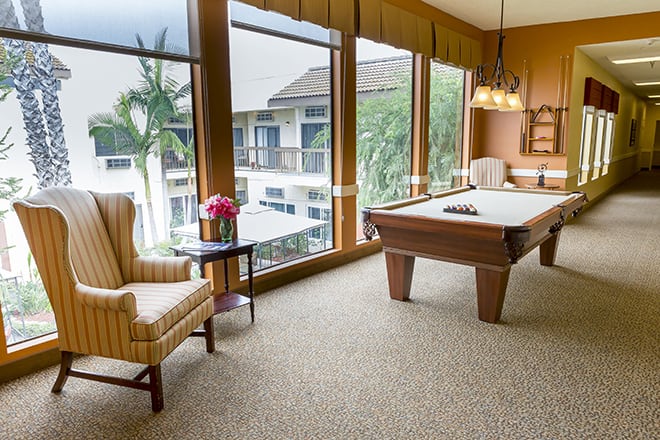 A well-lit game room featuring a billiards table, comfortable seating, and large windows with a view.