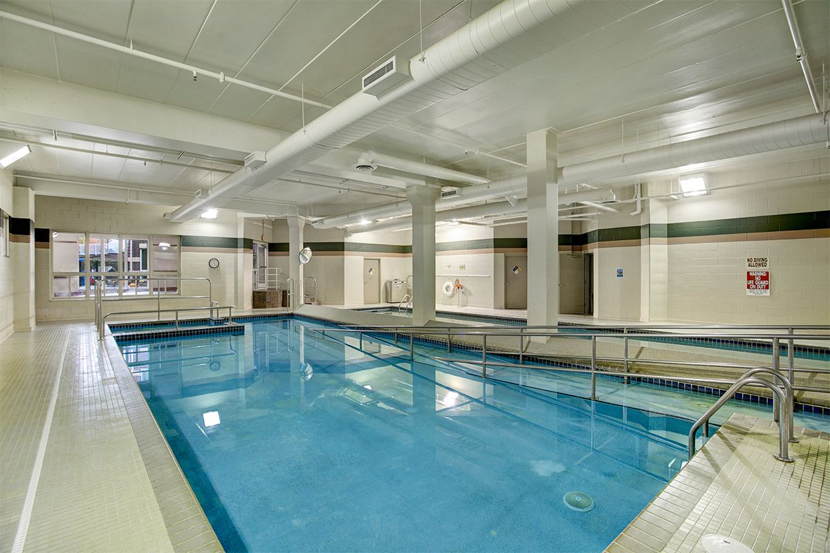 An indoor swimming pool surrounded by tiled flooring and overhead lighting.