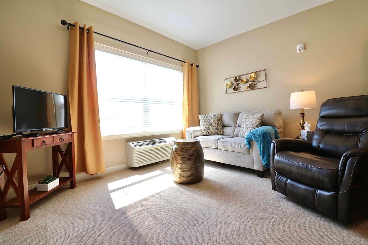 A cozy living room with a sofa, armchair, and a large window letting in natural light.